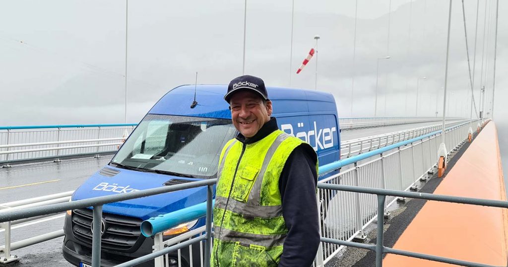 Bildet viser en smilende mannlig montør fra Böcker på Hardangerbroen foran en blå varebil.