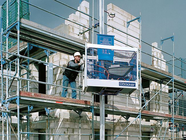 Mann i stillas tar imot S225 materialheis fra Böcker som er lastet med en trillebår. Fotografi fra produsenten.