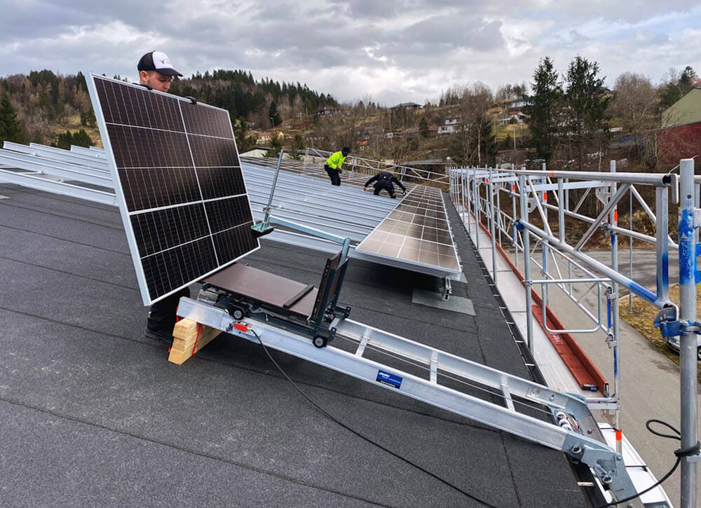 Solcellepanel er ankommet taket med toplift. Ansatt løfter solcellepanelet av solcelleplatformen.